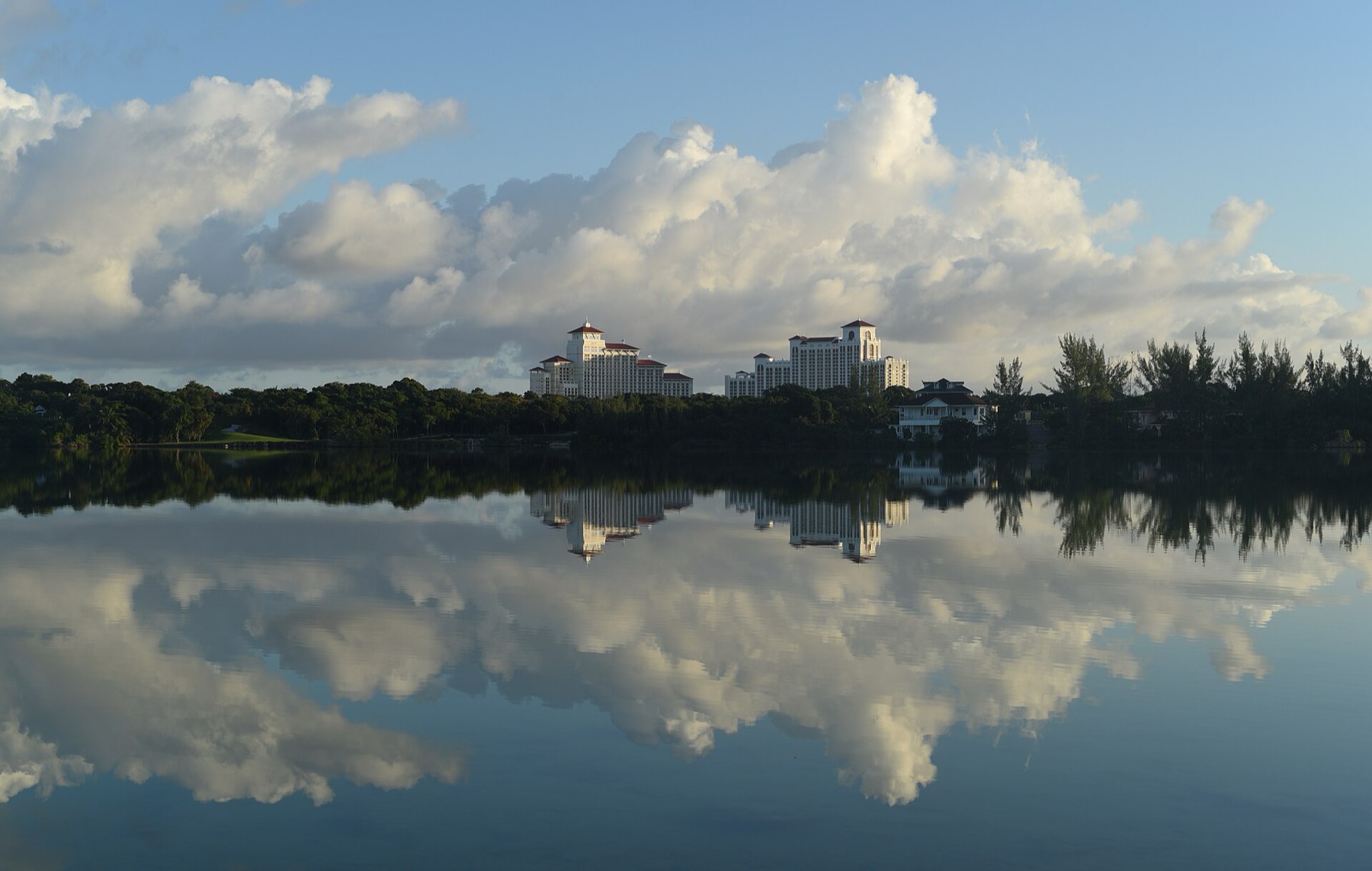 The cream-colored hotel towers of Baha Mar reflected in still water under towering clouds on New Providence, The Bahamas