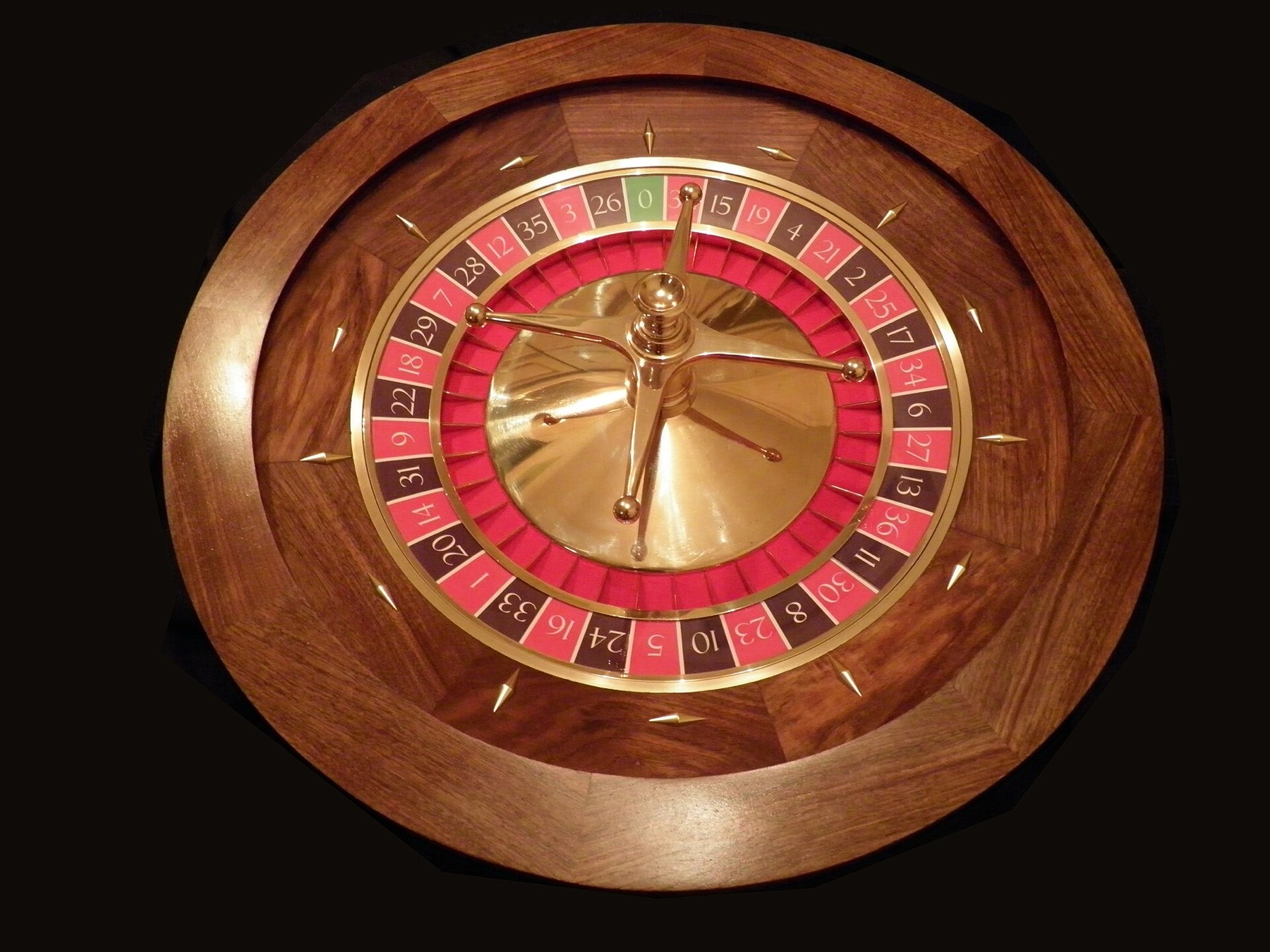 A polished wooden roulette wheel with red and black numbered pockets and a single green zero